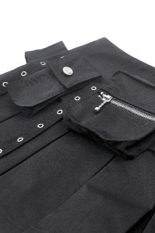 Close-up of black techwear mini skirt showing two utility pockets — one with a flap and snap button, the other with a zipper and eyelet trim.