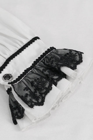 Close-up of white Victorian shirt cuff with black lace ruffle, ornate black button, and trim